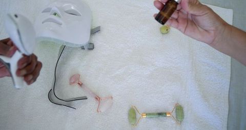 Esthetician preparing facial with led mask, jade and rose quartz rollers, senior client