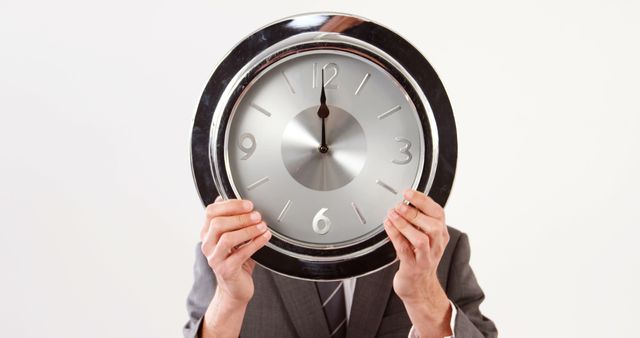 A Caucasian middle-aged businessman holds a large clock in front of his face, with copy space. His action suggests a focus on time management or the concept of time in business.