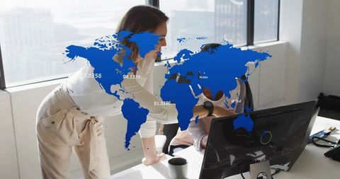 Female leader pointing at monitor while collaborating with coworker under digital world map