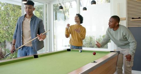 Diverse friends playing pool in game room, laughing and socializing with cues and drinks
