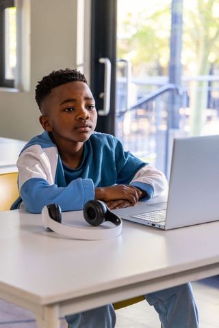 African american boy studying on laptop in bright modern classroom with headphones