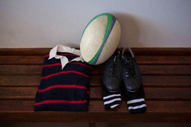 High angle view of rugby ball and clothes with shoes on bench in locker room