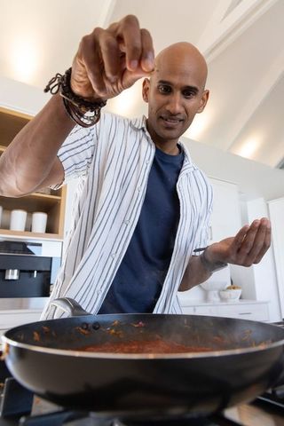 Indian man seasoning tomato sauce in contemporary kitchen, home cooking and flavor