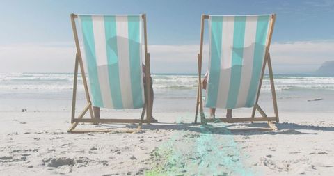 Mature couple relaxing in striped deck chairs on sunlit sandy beach