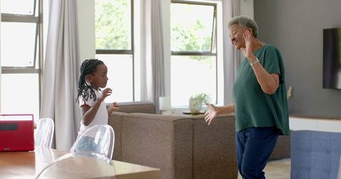 African american senior woman and girl dancing to music from red speaker in sunlit living room