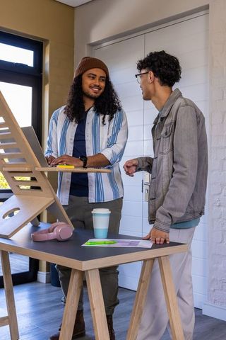 Two diverse male coworkers collaborating at standing desk with laptop in minimalist workspace