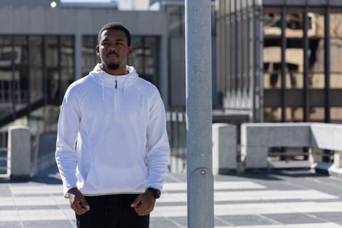 African american man standing on rooftop wearing white hoodie and watch, urban cityscape