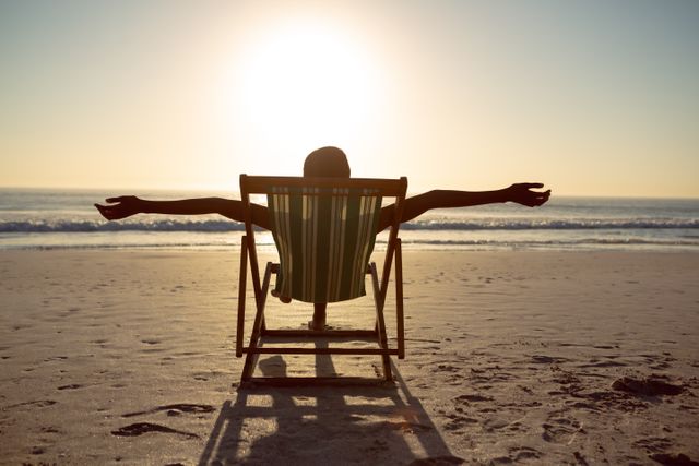 Rear view of woman relaxing with arms outstretched in a beach chair on the beach