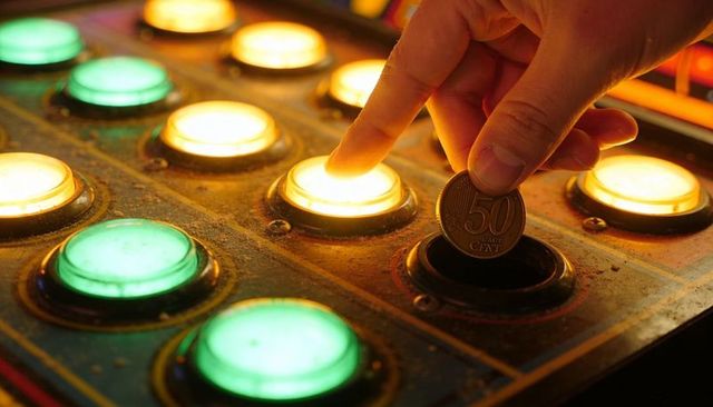 Finger pressing lit arcade button while dropping 50 cent coin on vintage game panel