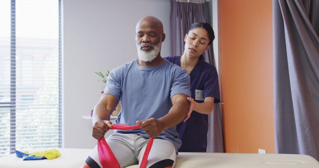 Senior man receiving physical therapy from a healthcare professional. The elderly patient is performing a resistance band exercise under the guidance of the therapist. Ideal for illustrating physical therapy practices, senior care therapies, rehabilitation processes, and healthcare services.