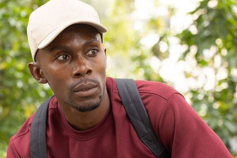 Young man wearing beige cap and burgundy sweatshirt looking right in leafy park portrait