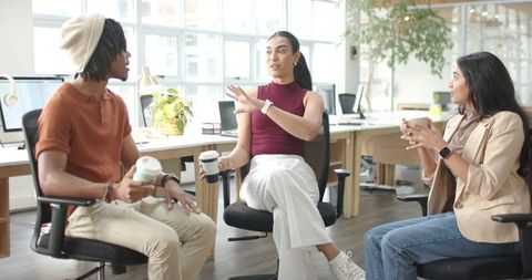 Diverse coworkers collaborating and sharing ideas over coffee in sunlit open-plan office