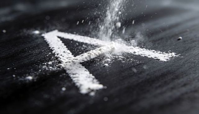 Sprinkling fine white powder forming letter a on dark slate surface with motion dust