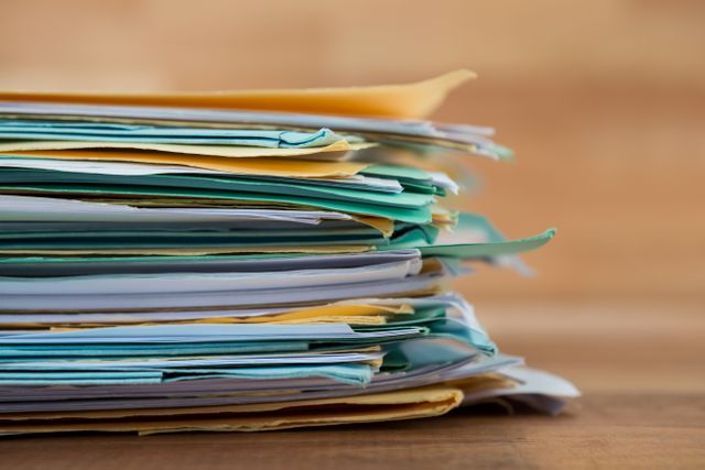 Close-up view of a stack of files on a table, ideal for illustrating concepts related to office work, organization, and paperwork management. Useful for business presentations, administrative content, and office supply advertisements.