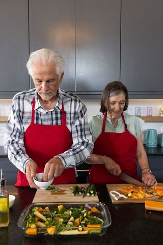 Senior couple cooking together wearing red aprons in modern kitchen