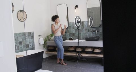 African american influencer filming skincare tutorial in modern bathroom with ring light