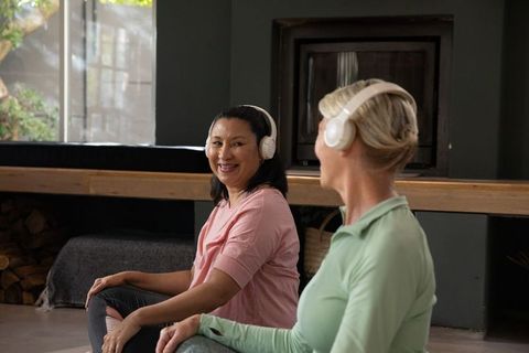 Two women practicing guided meditation with wireless headphones in cozy living room wellness session