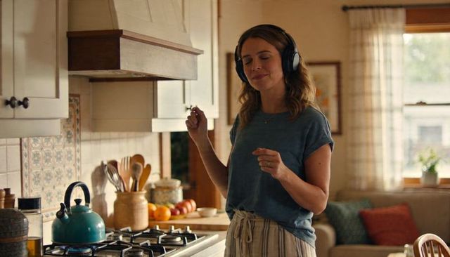 Woman wearing headphones listening to music in sunlit cozy kitchen, swaying by stove