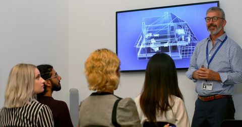 a professional instructor is engaging a diverse group of young adults in a presentation discussing architectural plans displayed on a screen. ideal for illustrating concepts of education, workshops, diversity in professional environments, teamwork in architecture, or seminars focused on architectural design and urban planning.