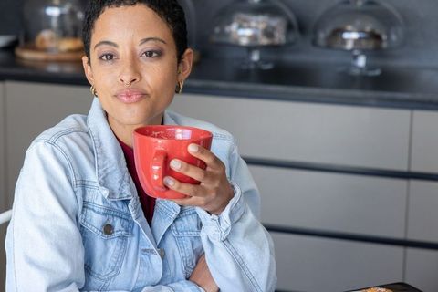 Contemplative african american woman sipping coffee at cafe counter holding red mug