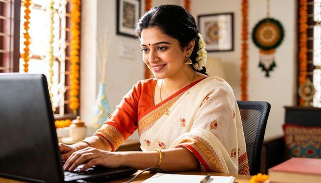 Smiling woman working on laptop in cream saree with jasmine flowers and marigold decor