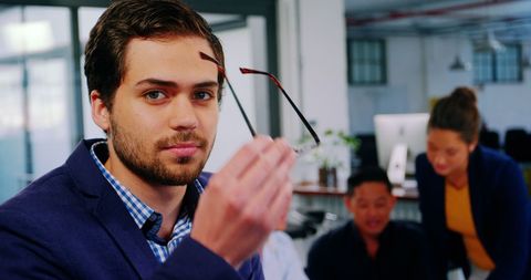 Confident young businessman holding glasses in modern office