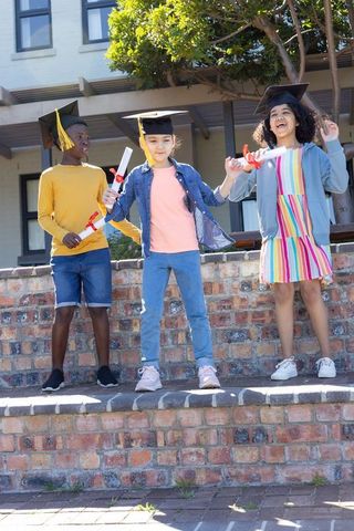 Multicultural children celebrating graduation outdoors with mortarboards and diplomas