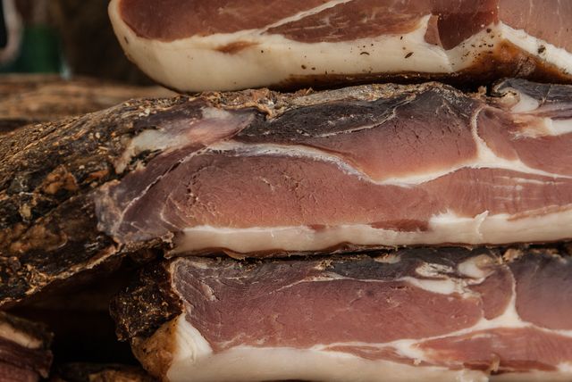 Close-up of cured ham showcasing marbled texture and rich colors. Ideal for use in food blogs, cooking magazines, gourmet product advertisements, and charcuterie-related content.