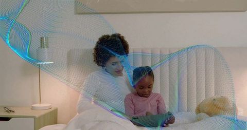 Mother and daughter sharing tablet in cozy bedroom with glowing digital mesh overlay