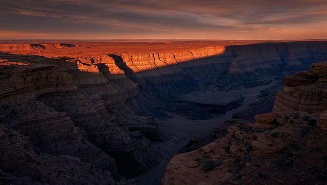Sunlit canyon rim casting deep shadows over vast sandstone gorge during sunset light