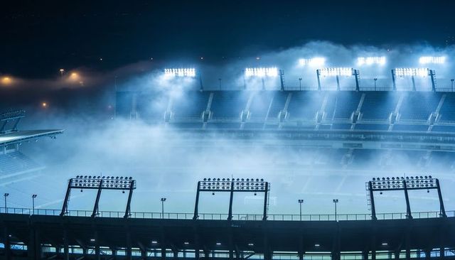 Misty night stadium floodlights casting blue glow over empty arena