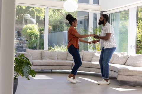 African american couple dancing in sunlit contemporary living space with floor-to-ceiling windows