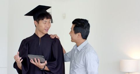 Father Congratulating Graduate Son in Cap and Gown at Home