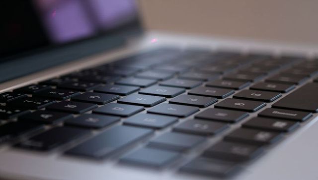 Chiclet laptop keyboard shallow focus showing key cluster with metallic deck, purple light