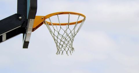 Outdoor basketball hoop with bright orange rim and white net against cloudy sky