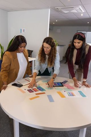 Female coworkers collaborating on color palettes and app mockups around round table