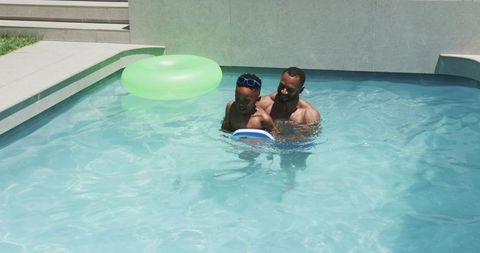 Father teaching young son to swim with kickboard in sunny backyard pool family bonding