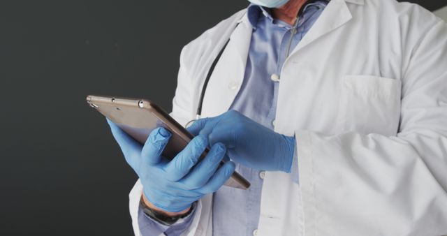Mid section of caucasian male doctor wearing surgical gloves using digital tablet. distant communication and telemedicine consultation concept.