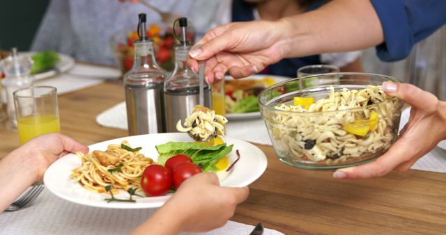 Family members sharing a bowl of healthy pasta salad at a dinner table. The scene includes a bowl of fresh salad with pasta, cherry tomatoes, and leafy greens. Ideal for illustrating concepts of healthy eating, family gatherings, home-cooked meals, and communal dining.