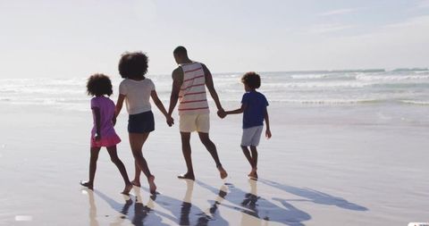 Family walking on beach holding hands with wet sand reflections and gentle ocean waves