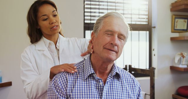 Chiropractor treating senior male patient by massaging neck in sunlit clinic room. Senior patient looks relaxed while undergoing treatment. Ideal for topics related to healthcare, chiropractic therapy, senior wellness, and pain relief.