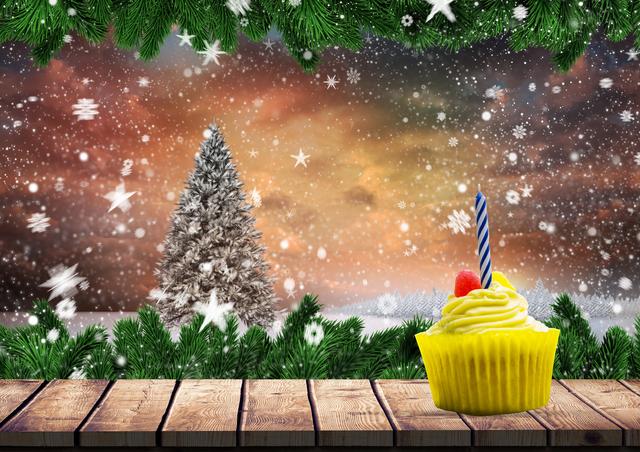 Cupcake with yellow frosting and candle on wooden plank under green branches, surrounded by snowflakes and a snow-covered Christmas tree in background. Perfect for holiday-themed advertisements, greeting cards, digital designs, and winter celebration promotions.