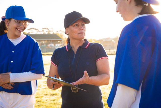 Female baseball coach discussing game tactics with her team on an outdoor field. Ideal for use in articles about women in sports, coaching strategies, teamwork, and athletic training programs. Can also be used for promoting sports events, team-building activities, and leadership in sports.