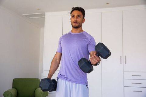 Focused indian man doing dumbbell curls in home gym setting