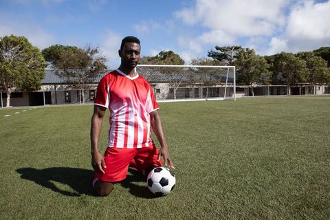 Soccer Player Kneeling with Ball on Green Field Wearing Red Jersey