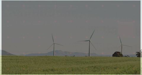 Wind turbines generating clean energy over green crop field with rolling hills backdrop