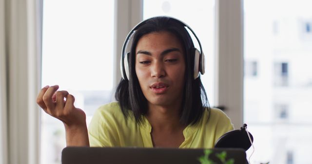Young woman with headphones working remotely on laptop, focusing on task at hand. Ideal for illustrating concepts related to remote work, telecommuting, technology use, home office setups, or modern work environments.