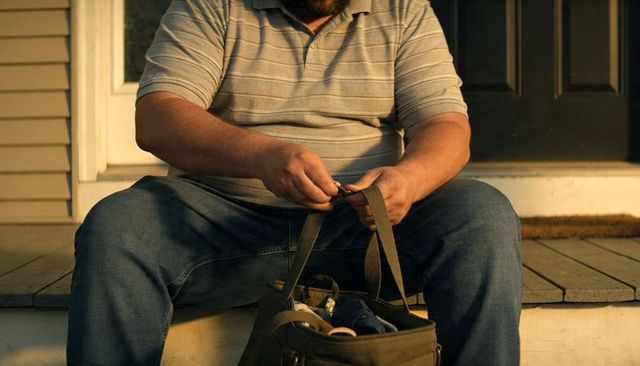 Handyman fastening canvas tool bag on front porch steps during warm golden-hour light