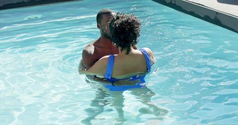 Sunlit pool romance kissing and embracing diverse couple in blue swimsuit, intimate moment