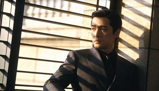 Businessman in suit gazing through blinds with dramatic sunbeam shadows and moody office